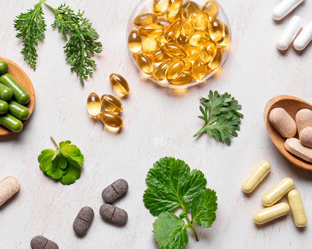 Ulike vitaminer som ligger på en benk, med ulike grønne blader.